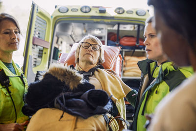 Paramedics with female mature patient on hospital gurney against ambulance