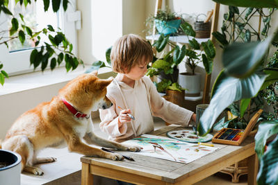 Cute male kid art drawing multicolored image use paints and brush on table at brightly room