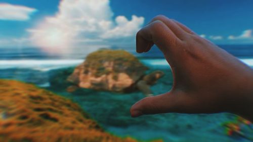 Cropped image of hand against sea against sky