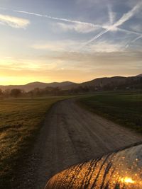 Road amidst field against sky during sunset