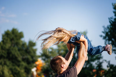 Low angle view of man and daughter against sky