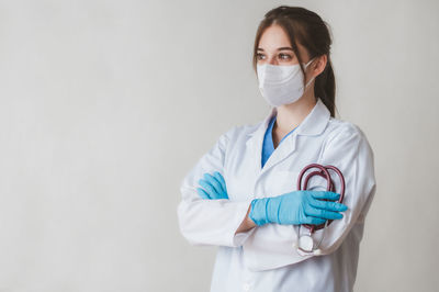 Doctor looking away while standing with stethoscope against white background