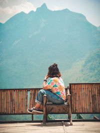 Rear view of woman sitting on bench against mountain