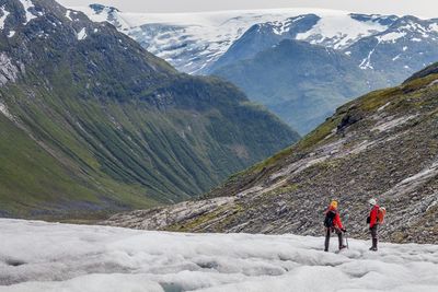 Rear view of hikers on glacier against rocky mountains