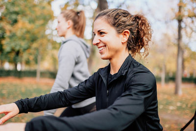 Smiling young woman sitting on tree during autumn
