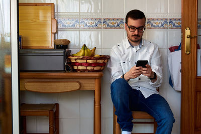 Young man looks at his phone sitting on a kitchen chair