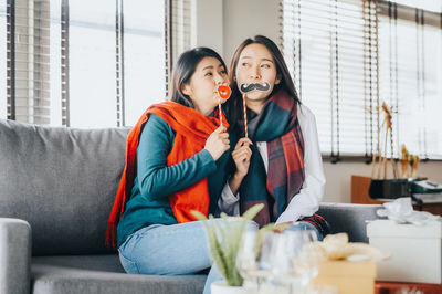 Woman holding party props while sitting on sofa at home