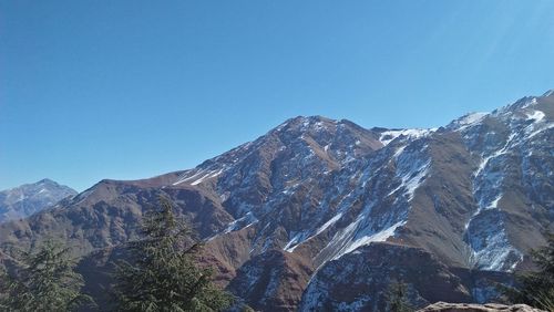 Low angle view of snowcapped mountains against clear blue sky