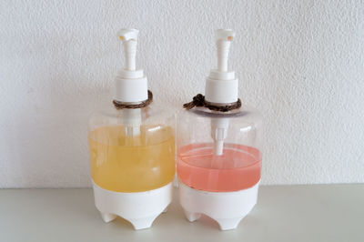 Close-up of soap dispensers on table by white wall