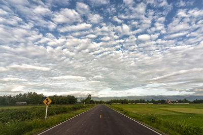 Road passing through field against sky