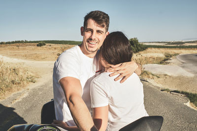 Girl hugs her boyfriend, while boy looks and smiles on camera