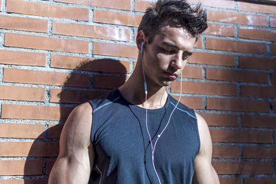 Man listening music standing against wall outdoors