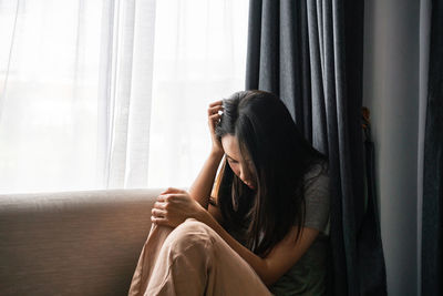 Side view of woman looking through window at home