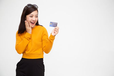 Young woman holding smart phone while standing against white background