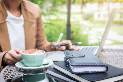 Midsection of woman with coffee cup using laptop on table at outdoor cafe