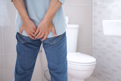 Midsection of man touching buttocks in bathroom