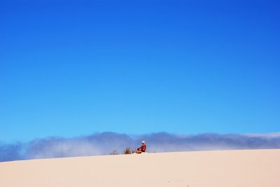 Man on sand dune in desert against blue sky