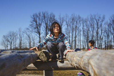 A child perches on wooden structure in park with father in background