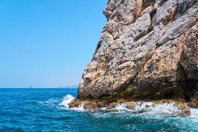 Rock formation in sea against clear blue sky