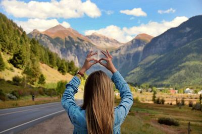 Rear view of young woman gesturing against mountains