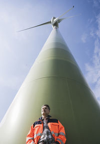 Engineer in front of tall wind turbine on sunny day