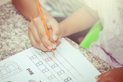 Cropped hand of parent assisting child writing on book at table