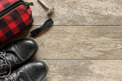 Directly above view of shoe by bowtie and razor with checked pouch on wooden table