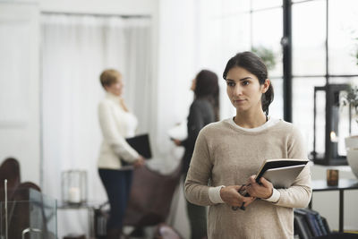 Thoughtful businesswoman holding laptop with colleagues in background