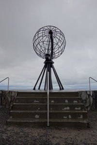 Metallic structure on bench against sky