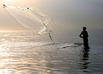 Man fishing in sea against sky during sunset