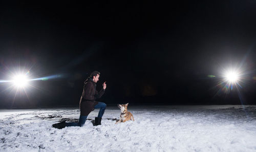 Man playing with dog on illuminated snow landscape