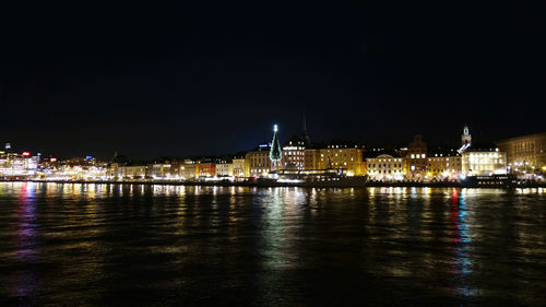 Illuminated buildings by river against sky at night