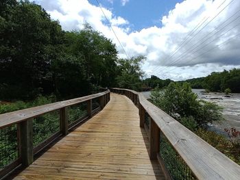 Footbridge over footpath amidst plants against sky