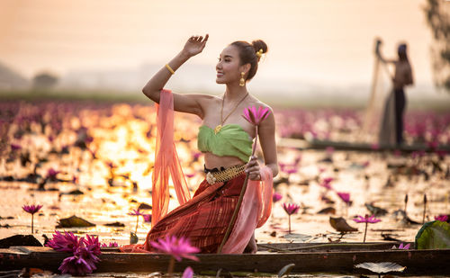 Young woman holding water lily in boat on lake during sunset