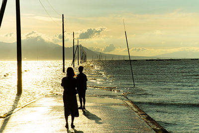 Rear view of people walking at beach against sky during sunset