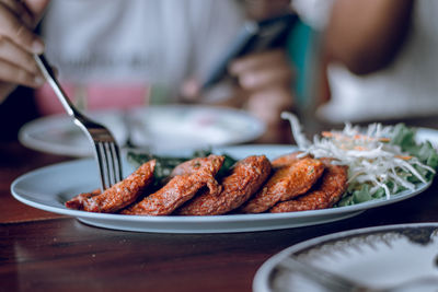 Cropped hand holding food using fork on table