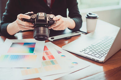 Midsection of interior designer holding camera with laptop on table