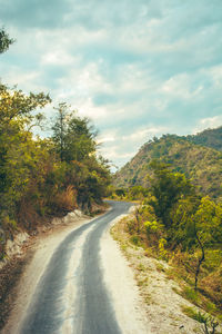 Road amidst trees and plants against sky