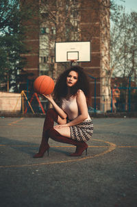 Portrait of beautiful young woman holding basketball on court