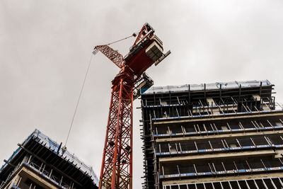 Low angle view of crane by building against sky