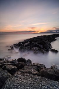 Rocks by sea against sky during sunset