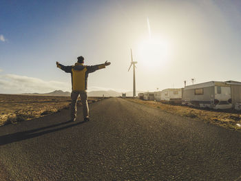 Rear view of man with arms outstretched standing on road against sky during sunset