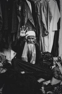 Portrait of senior man gesturing while sitting against clothes rack