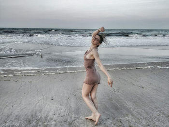 Portrait of woman posing while standing at beach against sky