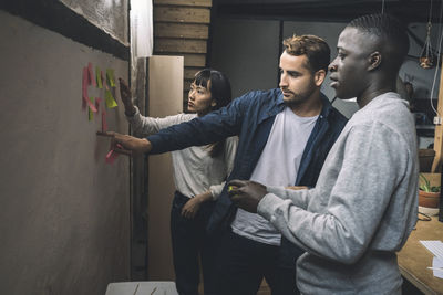 Male and female coworkers sticking adhesive note on wall at workplace