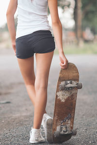 Rear view of woman with skateboard standing on footpath