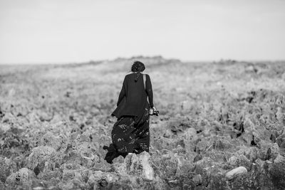 Rear view of man walking on field against clear sky