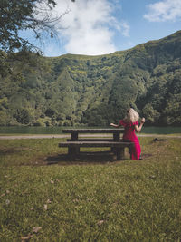 Rear view of woman sitting on bench against mountain at land