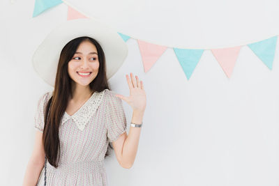 Portrait of a smiling young woman standing against white wall