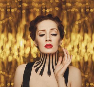 Redhaired girl with makeup and painted neck with a dramatic face expression on a golden background